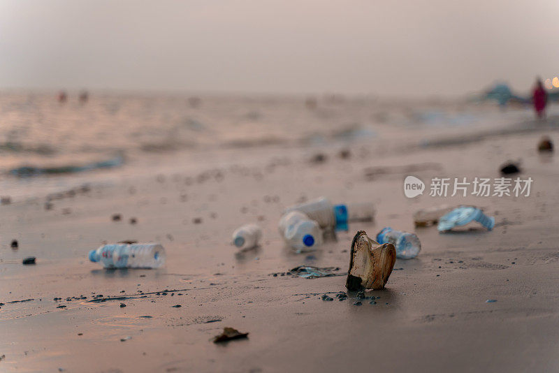 Low angle selective focus dirty beach with many consumer single used plastic waste along coast at twilight time. Environmental pollution micro plastic contamination problem concept.